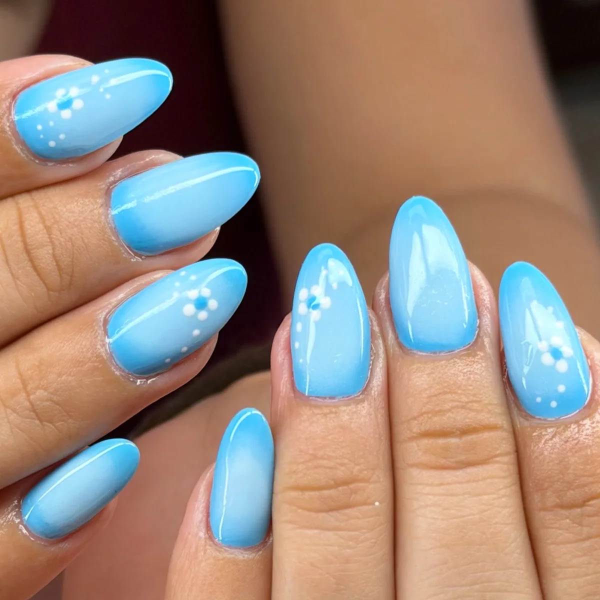 Almond nails in a sky-blue ombré, some with small white hand-painted flowers and dots