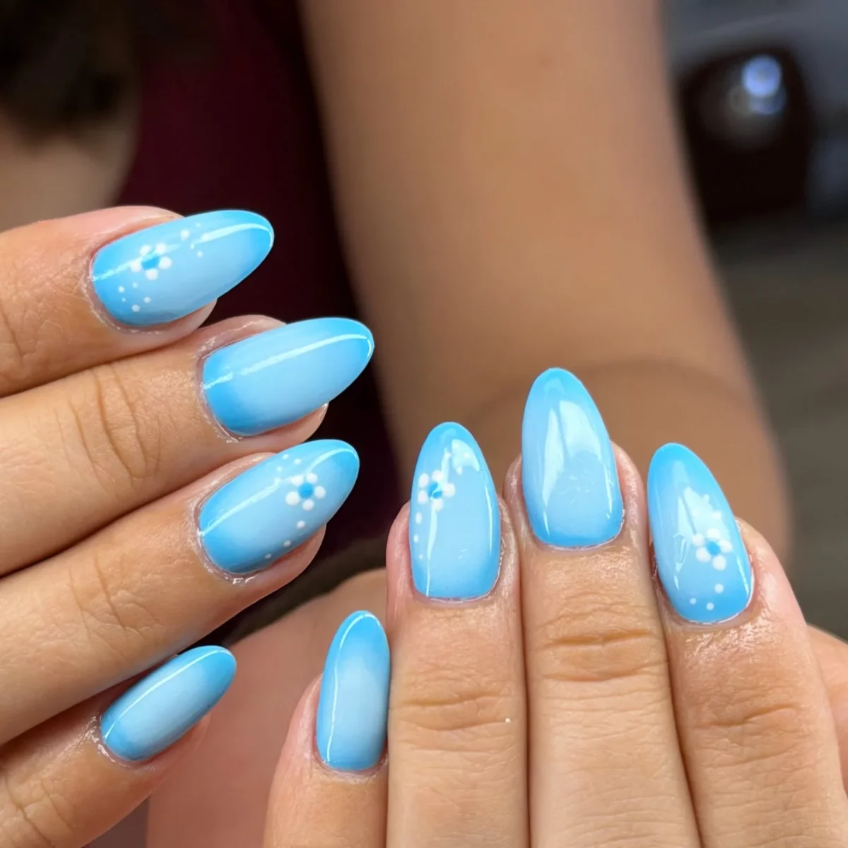 Almond nails in a sky-blue ombré, some with small white hand-painted flowers and dots