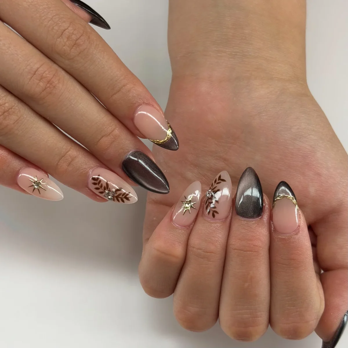 Almond nails in espresso-brown cat-eye, nude with cat-eye French tips edged in gold foil, brown hand-painted leaves with rhinestones, and gold star studs
