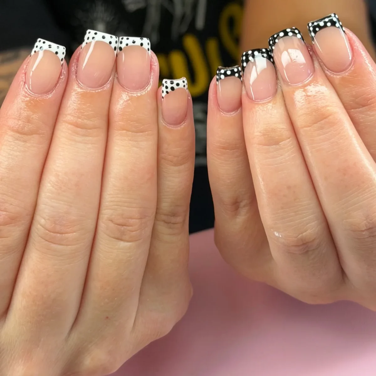Short square nails with polka-dot French tips: white with black dots on one hand, black with white dots on the other