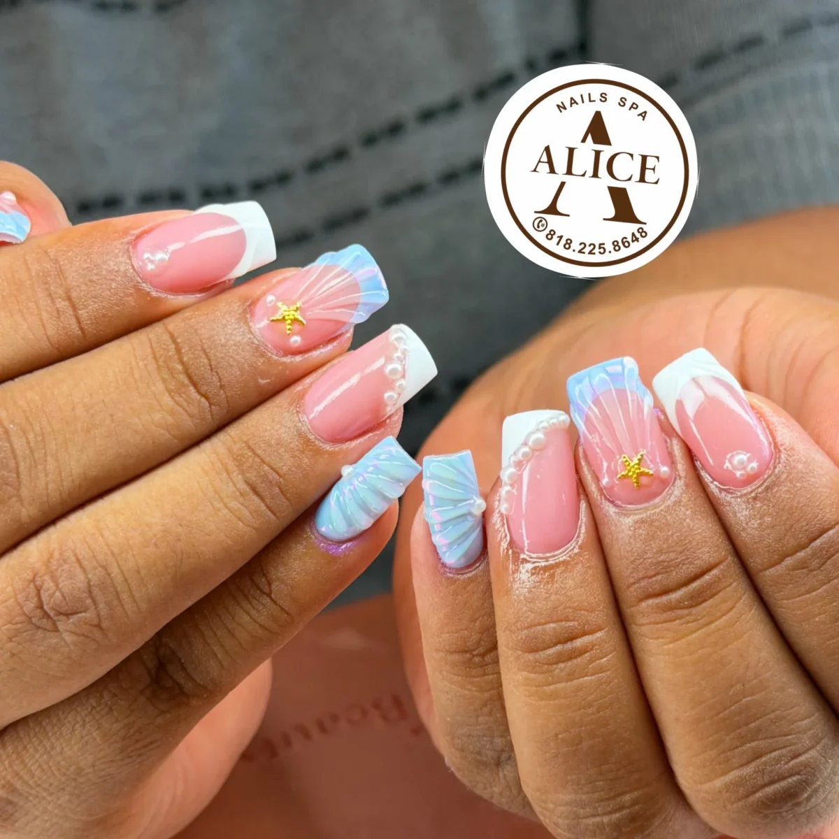 Square nails on a pink base: white French tips lined with pearls, pale blue iridescent 3D seashells and small gold starfish